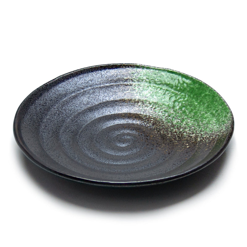 Black round porcelain plate with concentric ridges, fine speckling and a green accent on one rim sector.