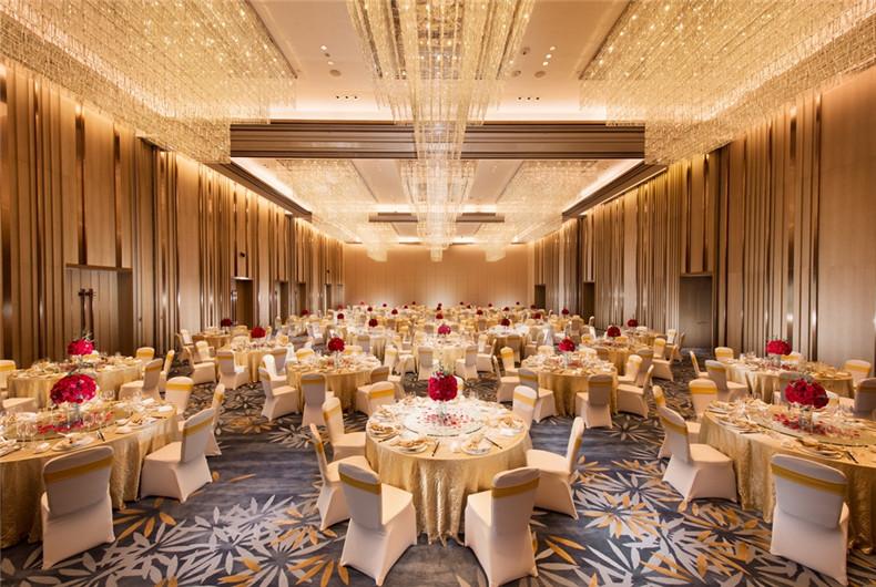 Banquet hall with round dining tables, cream-colored chairs and large ceiling chandeliers.
