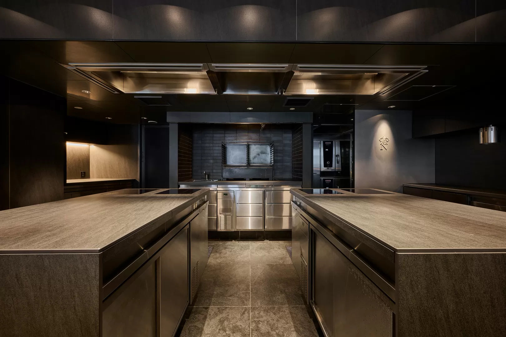Commercial kitchen with stainless-steel preparation counters and overhead ventilation.