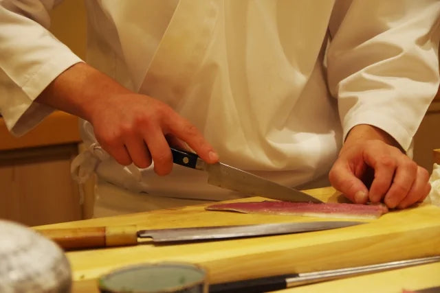 Sushi chef slicing a fish fillet beside Japanese knives on a cutting board
