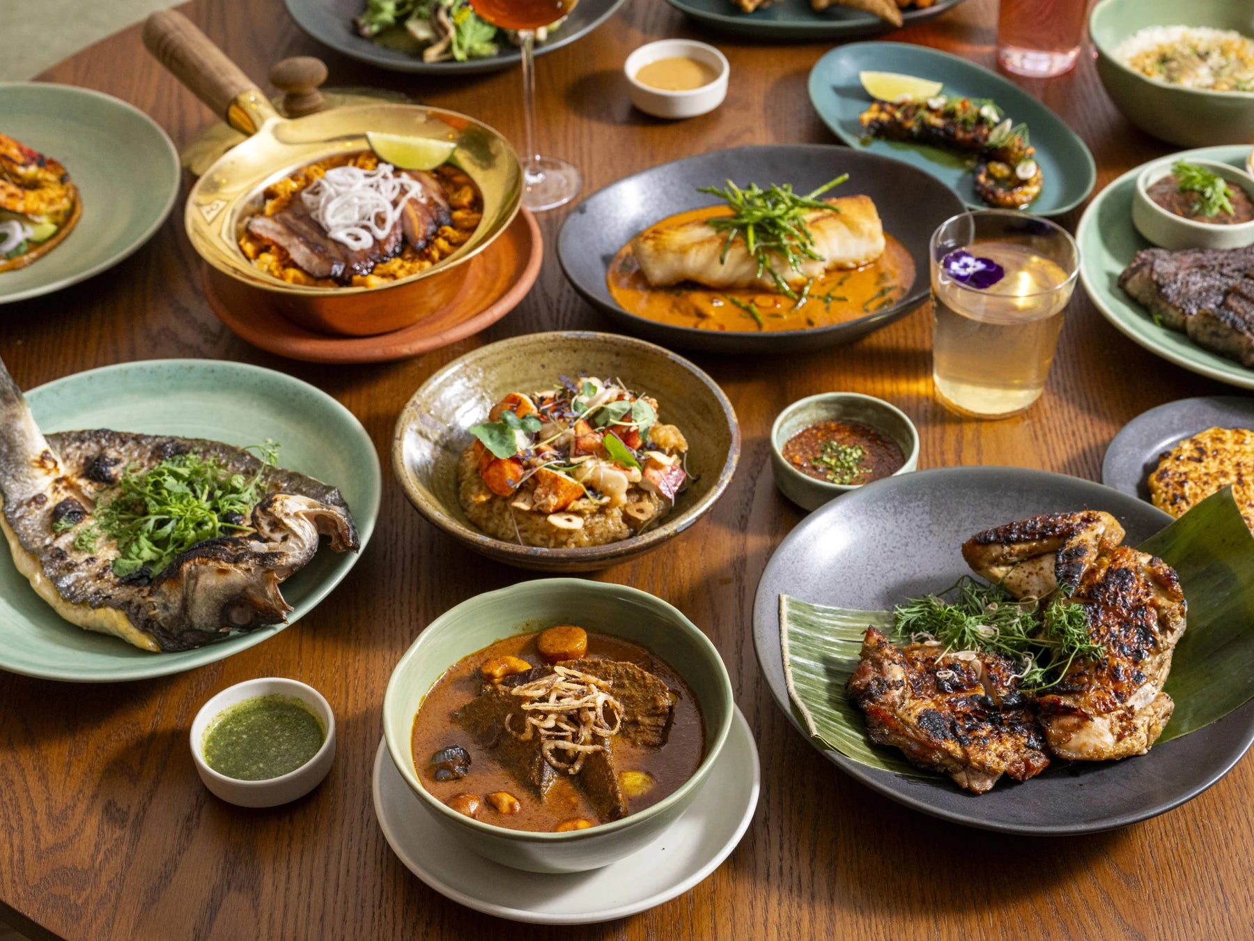 Shared Thai table with whole fish on an elongated platter, curry bowls, salad, rice and small sauce dishes.