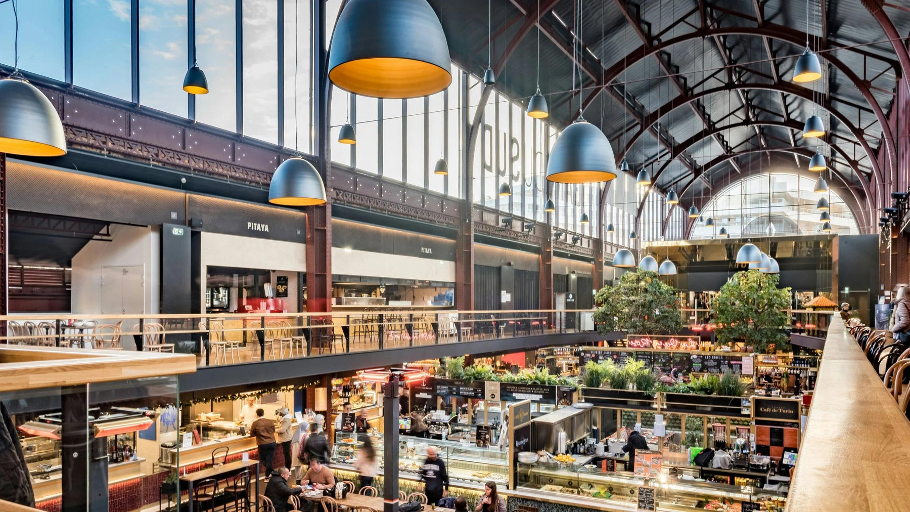 Indoor food hall with multiple vendor counters, communal seating and a high arched roof.