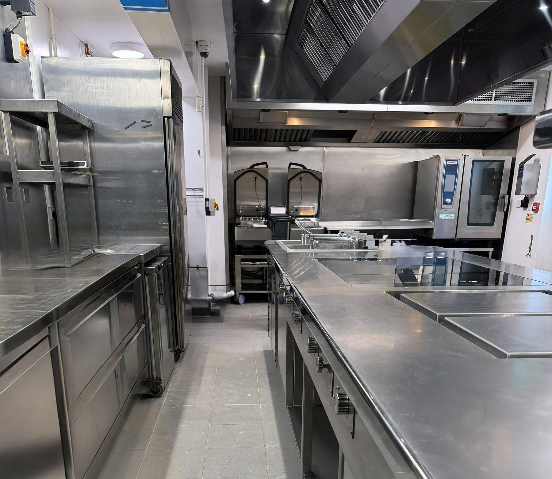 Commercial kitchen with stainless steel work counters, fryers, a combination oven and an exhaust hood.