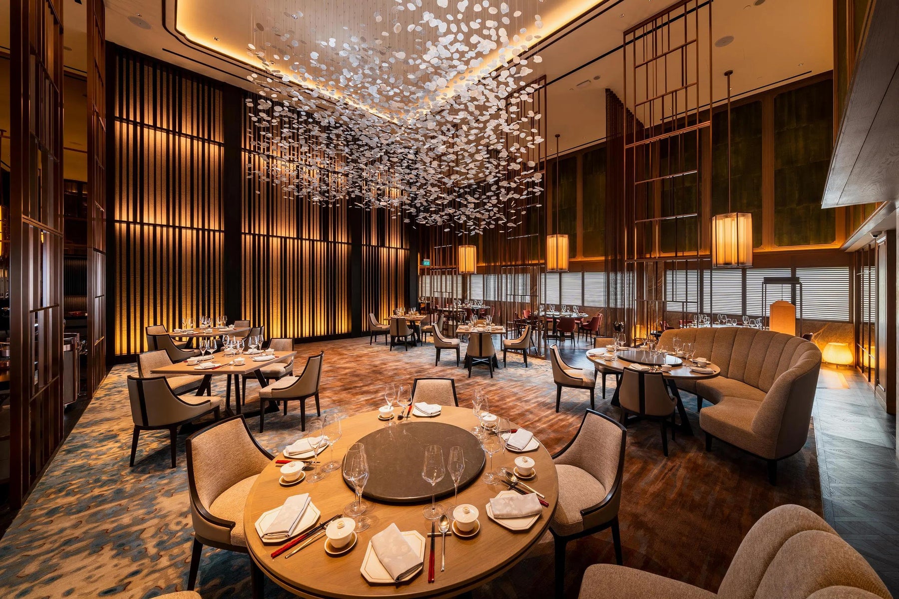 Hotel dining room with round tables, upholstered seating, timber wall panels and decorative lighting.