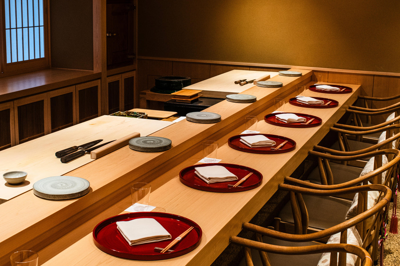 Repeated ceramic place settings along a wooden omakase counter