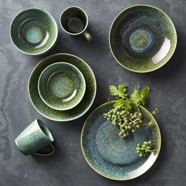 An overhead tabletop of green and dark mineral-toned plates, bowls and cups in related finishes.