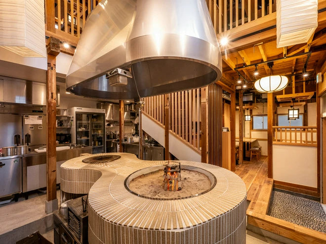 Specialty cooking station with a circular grill and suspended metal ventilation hood.