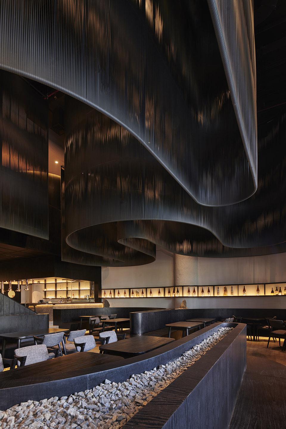Restaurant counter and dining space beneath a sculptural dark ceiling.
